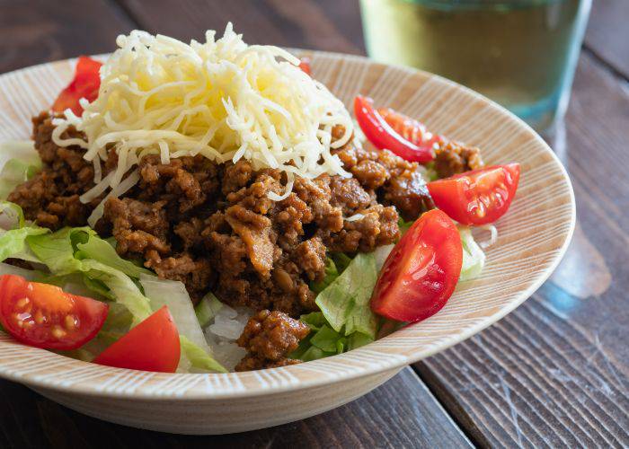 The Okinawan spin on taco rice, featuring spicy ground meat on top of a bed of rice, lettuce and tomatoes, sprinkled with cheese.